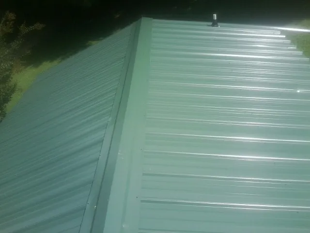New green metal panels meeting at the ridge of a roof — Flat Roof Repair work by our crew in Dunkirk